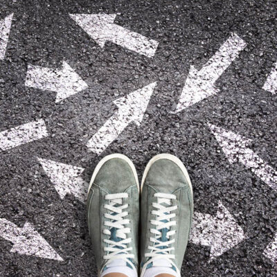 Sneaker shoes and arrows pointing in different directions on asphalt ground, choice concept